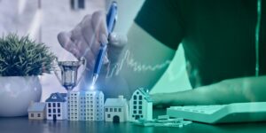 Miniature buildings, trophy, cash, and a hand with a pen overlaid by financial chart